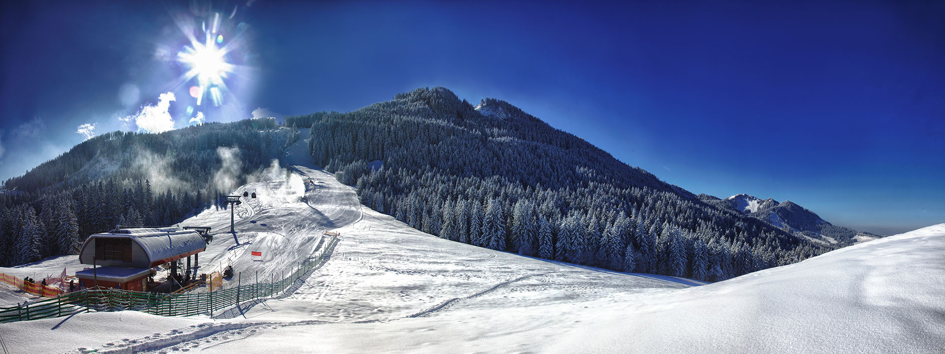 Skigebiet in der Morgendämmerung mit tief stehender Sonne über dem Grat