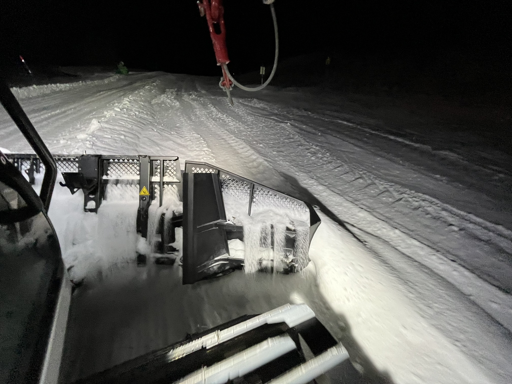 Blick aus der Fahrerkabine bei Nacht über das Räumschild auf die Piste