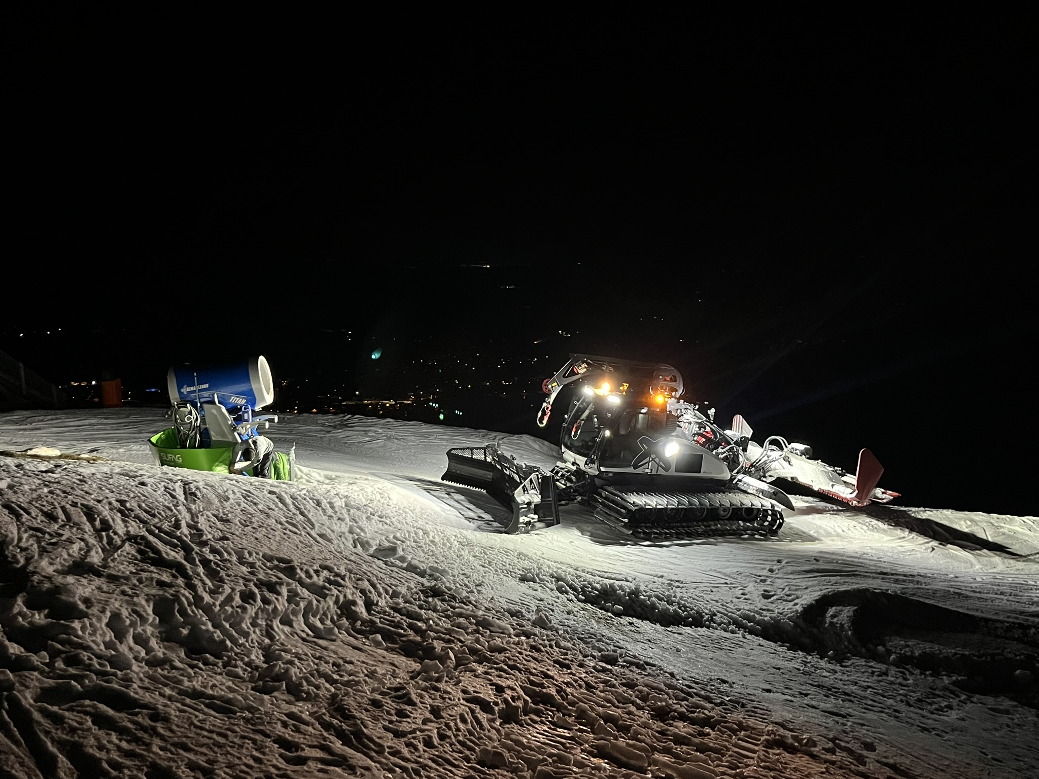 Zwei Pistenraupen bei Nacht auf einem schneearmen Hang
