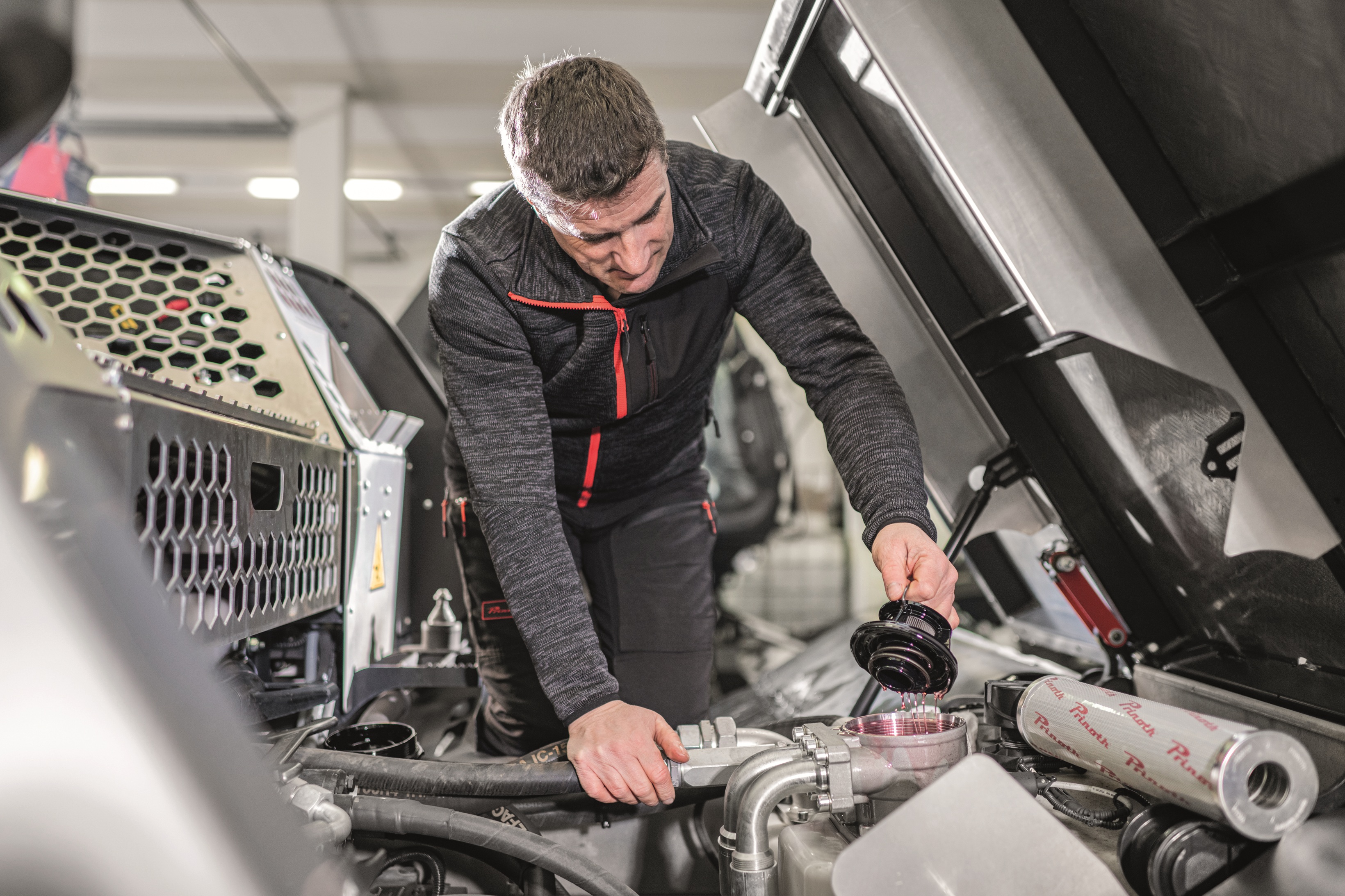 Techniker arbeitet am geöffneten Motorraum einer Pistenraupe in der Werkstatt