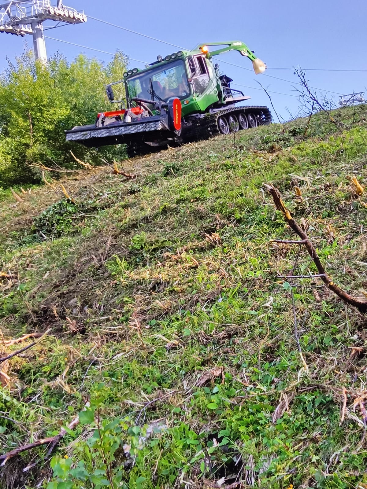 Pistenraupe mit Mähwerk im Sommereinsatz an einem grünen Steilhang