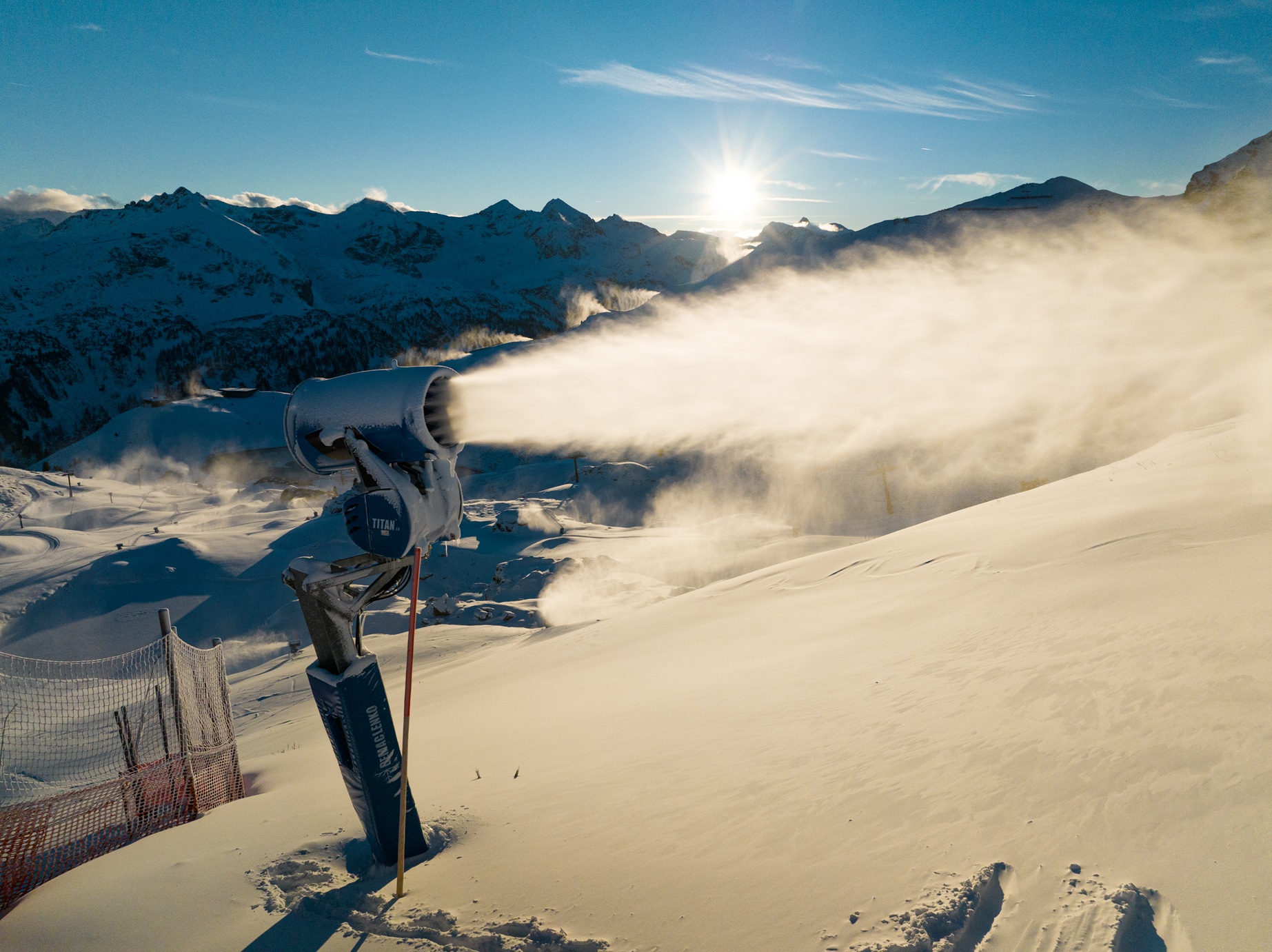 Beschneiungsanlage bei Sonnenaufgang, die Schneefahne weht über die Piste