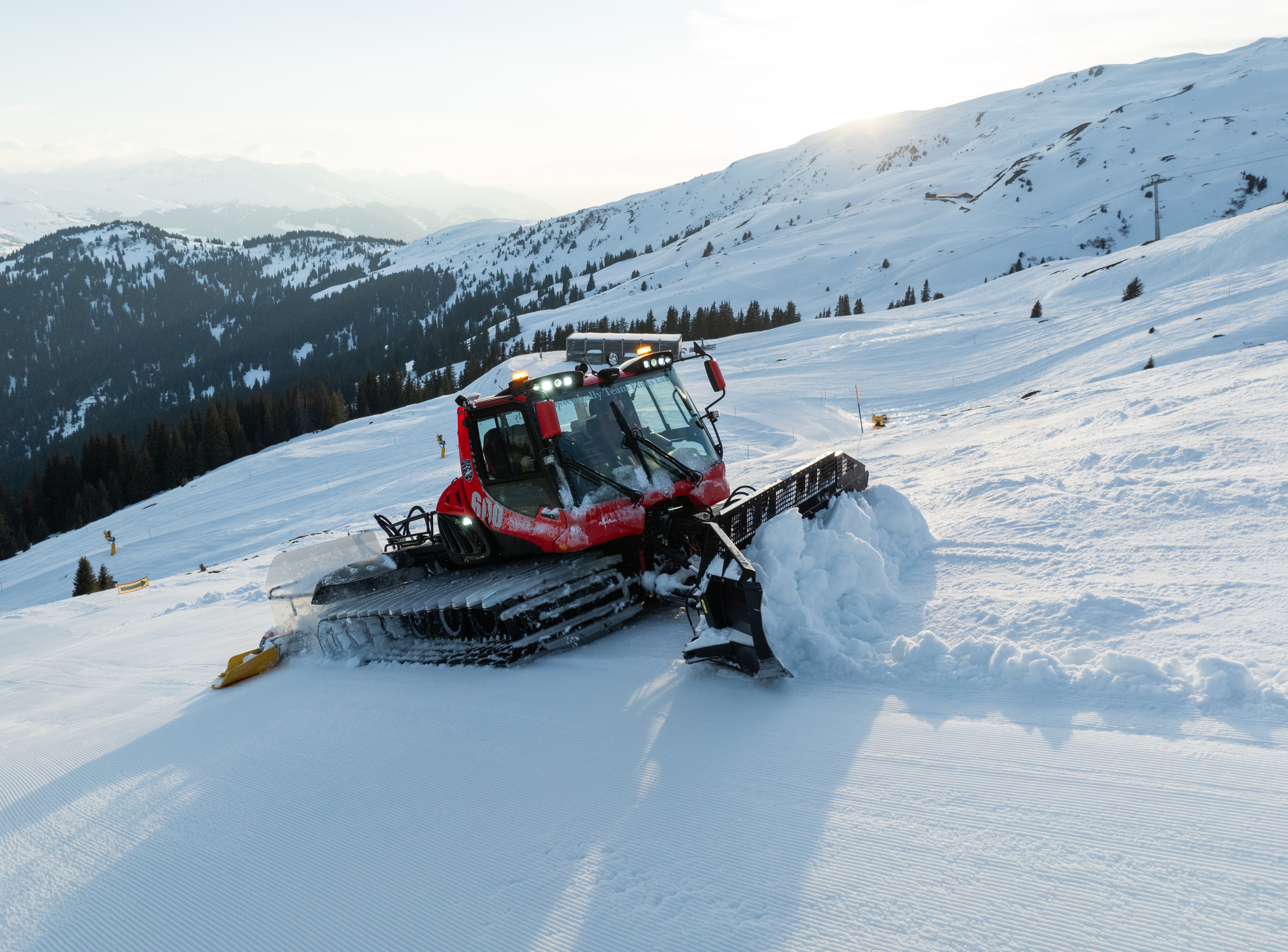 Pistenraupe schiebt Schnee auf einer weiten Piste bei Sonnenschein