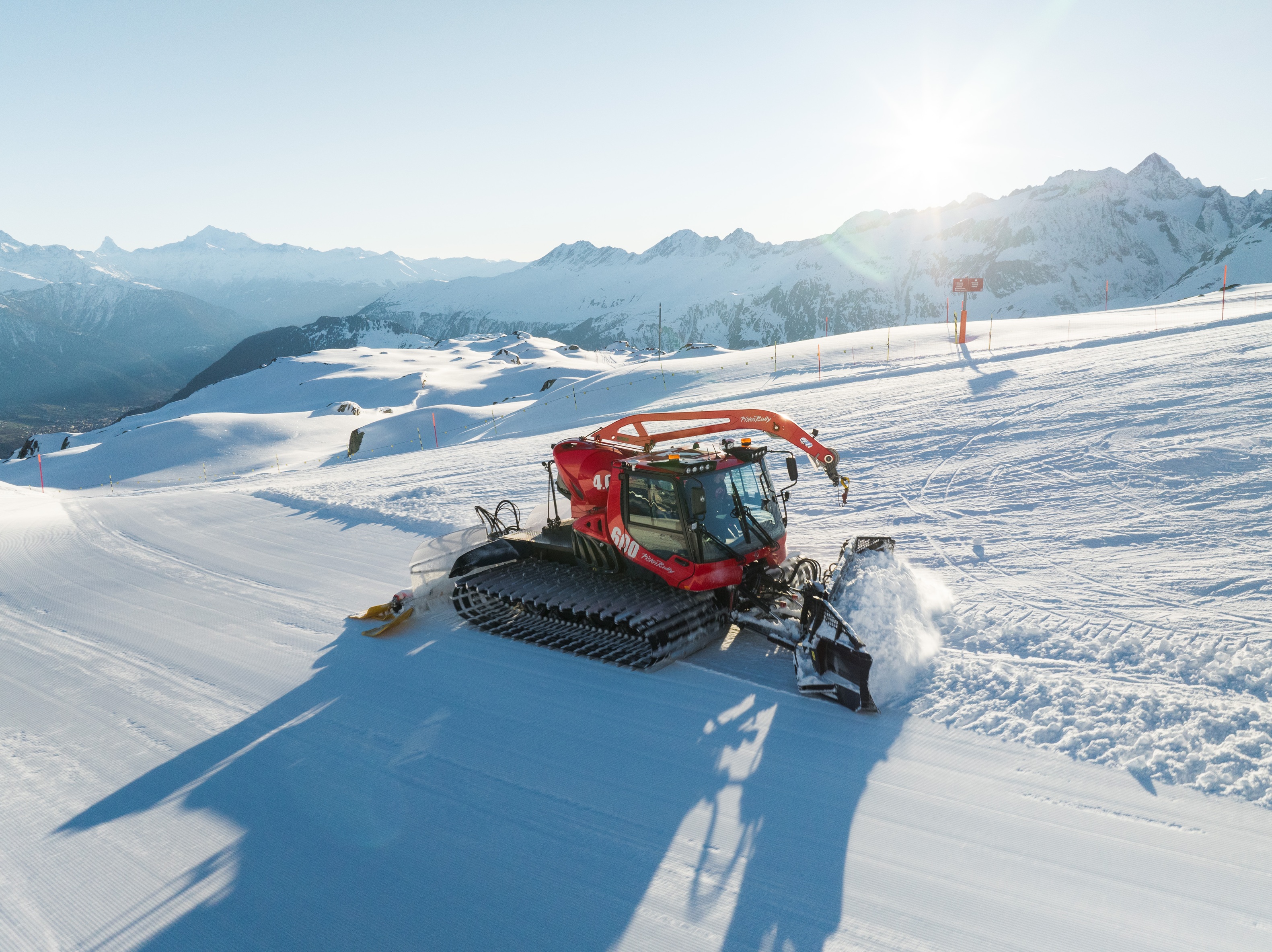 Pistenraupe auf präparierter Piste vor Bergpanorama im Gegenlicht