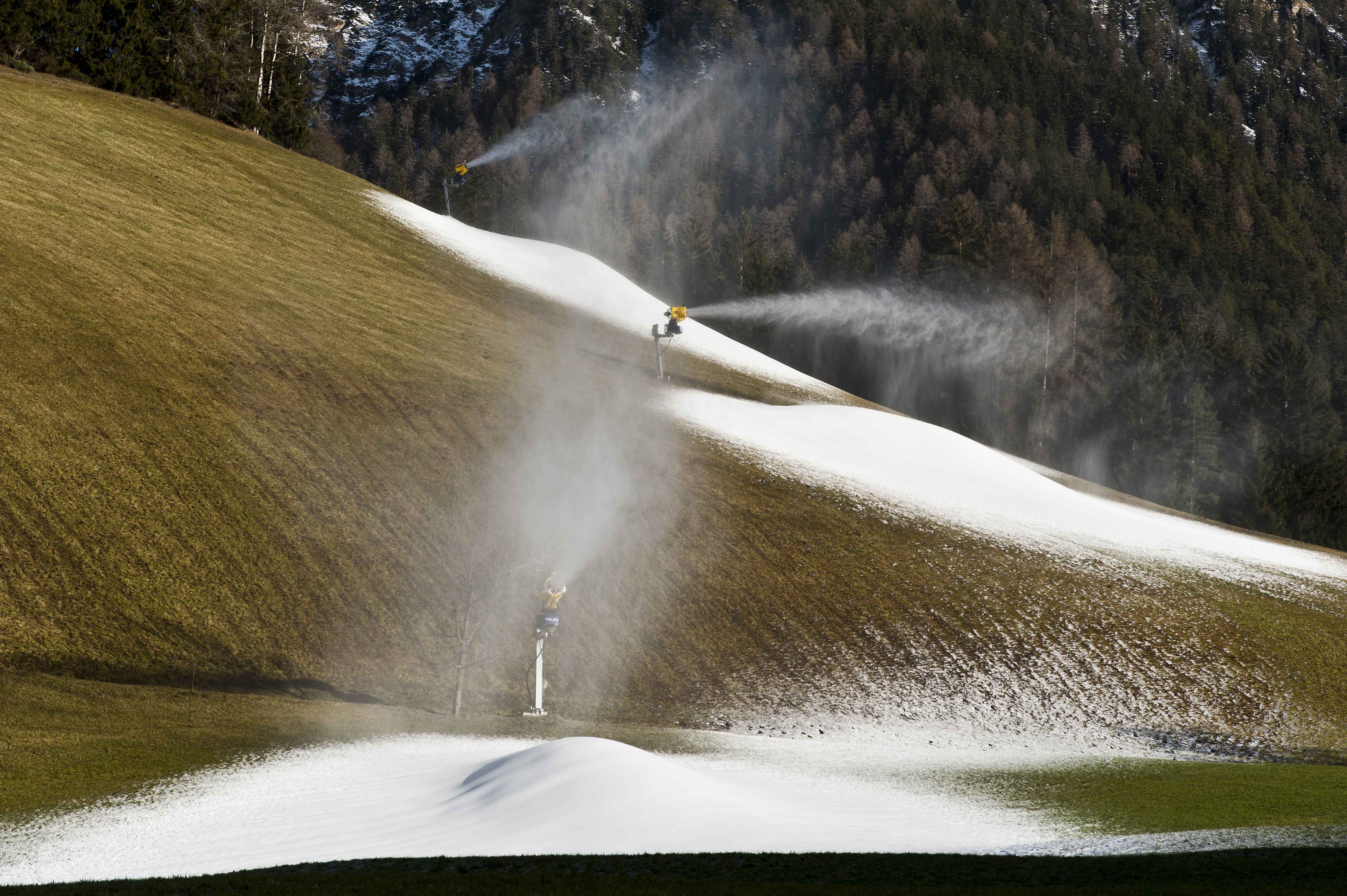 Schneekanone beschneit im Frühwinter einen noch grünen Hang